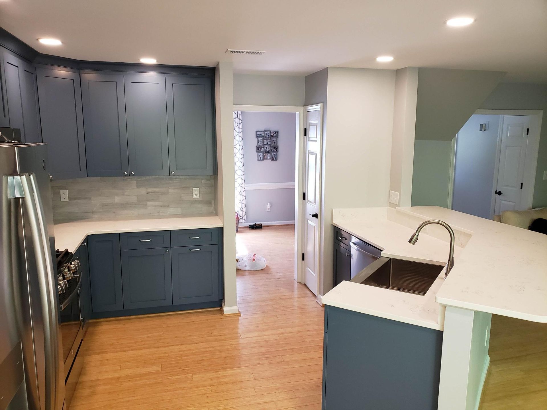Modern kitchen with blue cabinets, stainless appliances, white countertops, and wood floors