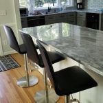 Modern kitchen with a marble island and two black bar stools on a wood floor