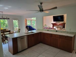 Open kitchen with dark wood cabinets, tile floor, ceiling fan, and large windows overlooking a living area.