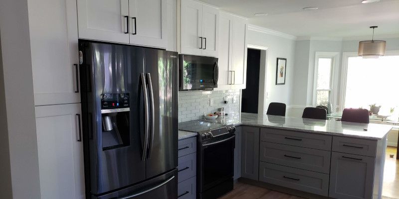 Modern white kitchen with black appliances, gray cabinets, and a breakfast island with stools