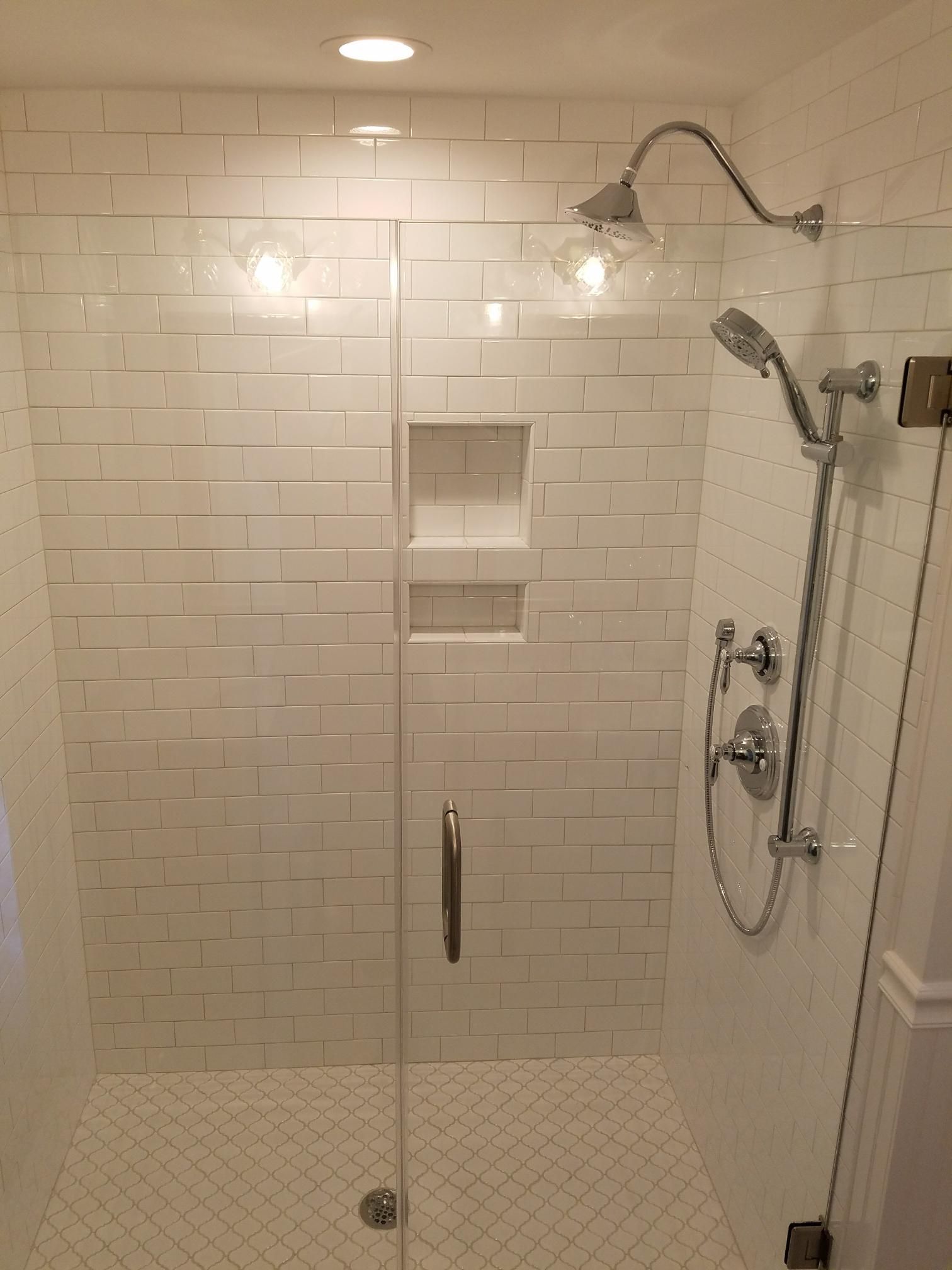 Glass shower stall with white subway tile, built-in niches, and chrome fixtures in a bright bathroom