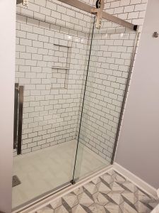 Glass shower enclosure with white subway tile walls and geometric tile floor outside
