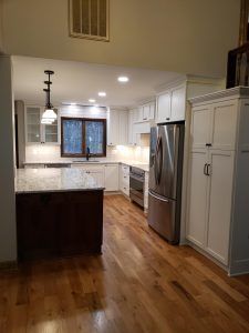 Modern kitchen with stainless steel fridge, white cabinets, hardwood floors, and granite island countertop