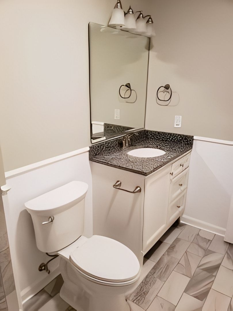 Small bathroom with toilet, vanity sink, mirror, and gray tile floor.
