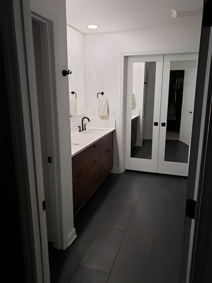 Modern bathroom with dark tile floor, white vanity, and mirrored cabinet doors.