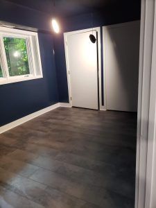 Empty room with dark blue walls, gray flooring, a window, and a white closet door with a round handle.