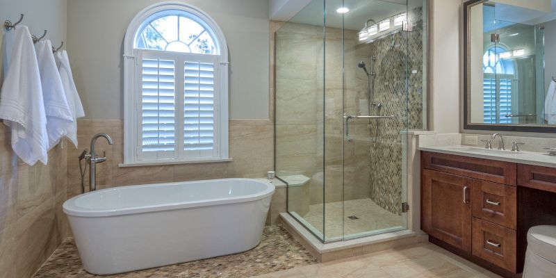 Modern bathroom with freestanding tub, glass shower, double vanity, and window with shutters