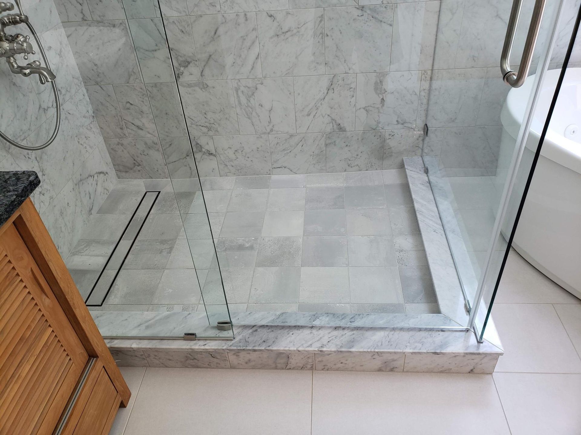 Glass shower enclosure with marble tile walls and a white tiled floor