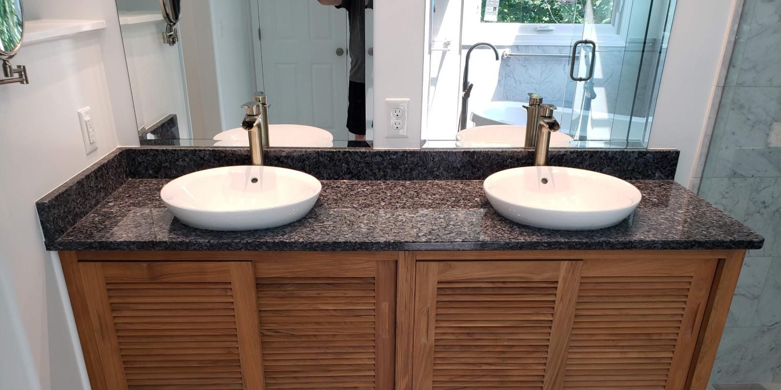 Bathroom vanity with two round sinks, brass faucets, and a granite countertop