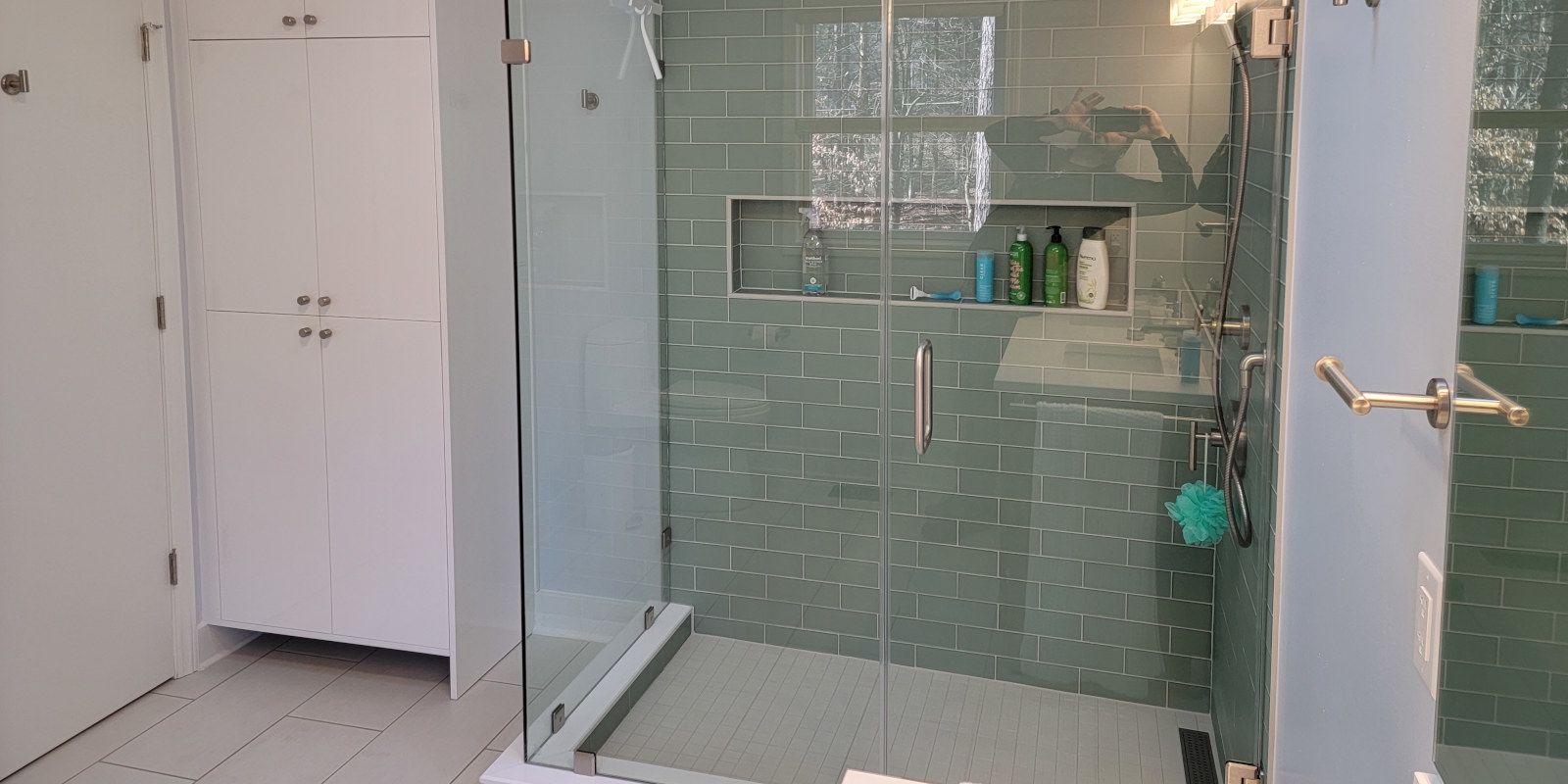 Bathroom with green tiled shower, white cabinets, and a glass door on the right