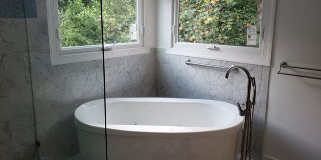 Bathtub beneath two windows in a tiled bathroom with a chrome shower fixture