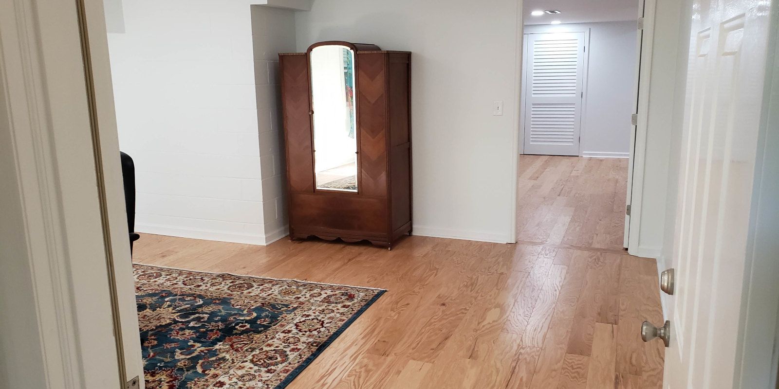 Empty hallway with wood floor, patterned rug, and a wooden cabinet near a doorway