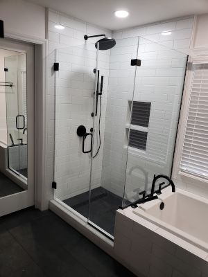 Modern white bathroom with glass shower, black fixtures, and a bathtub beside a wall mirror
