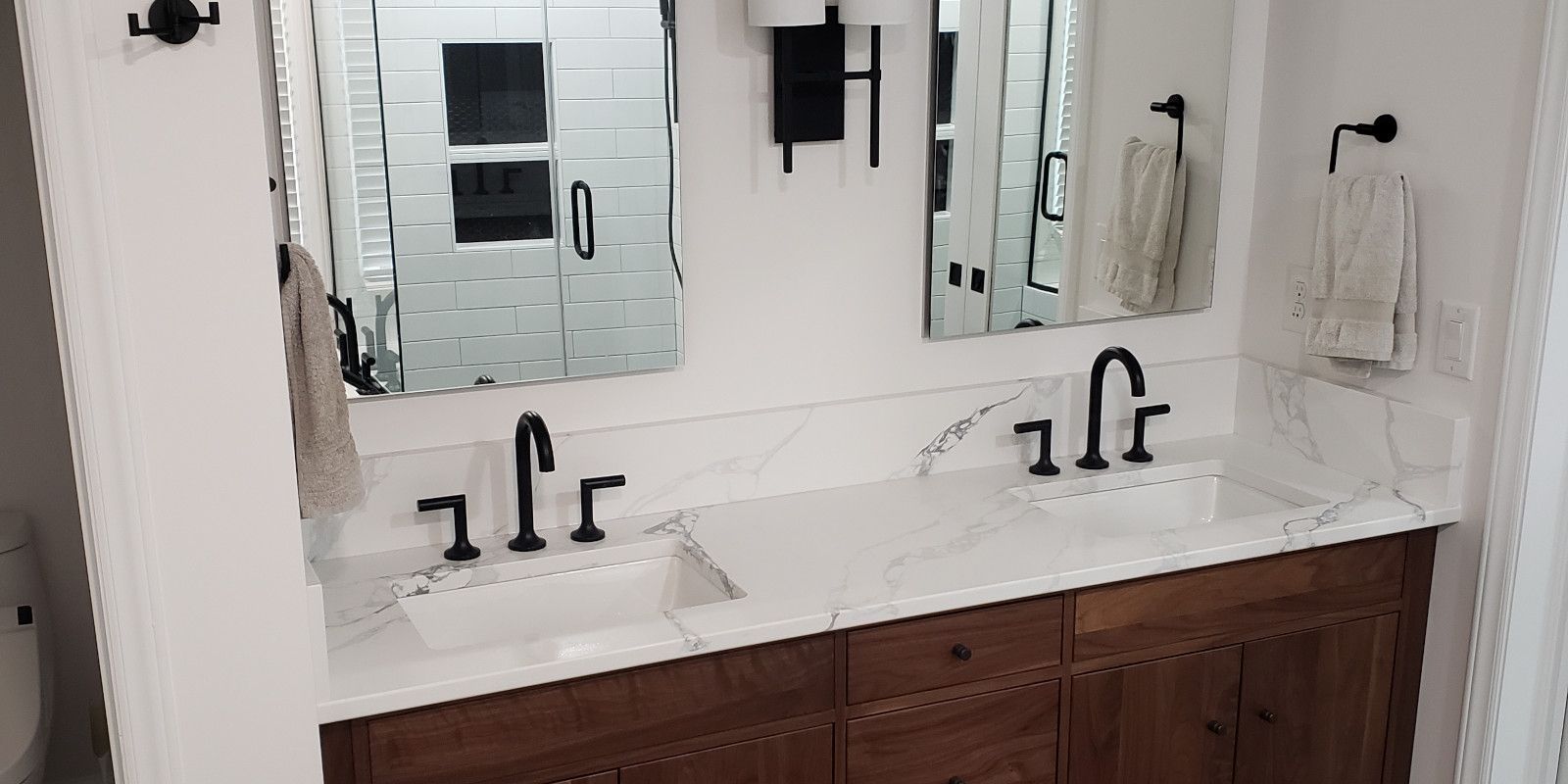 Double vanity bathroom with wood cabinets, marble countertops, and large mirrors.