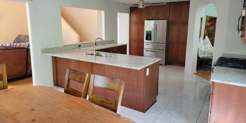 Modern kitchen with wood island, white tile floor, stainless fridge, and dining table in foreground