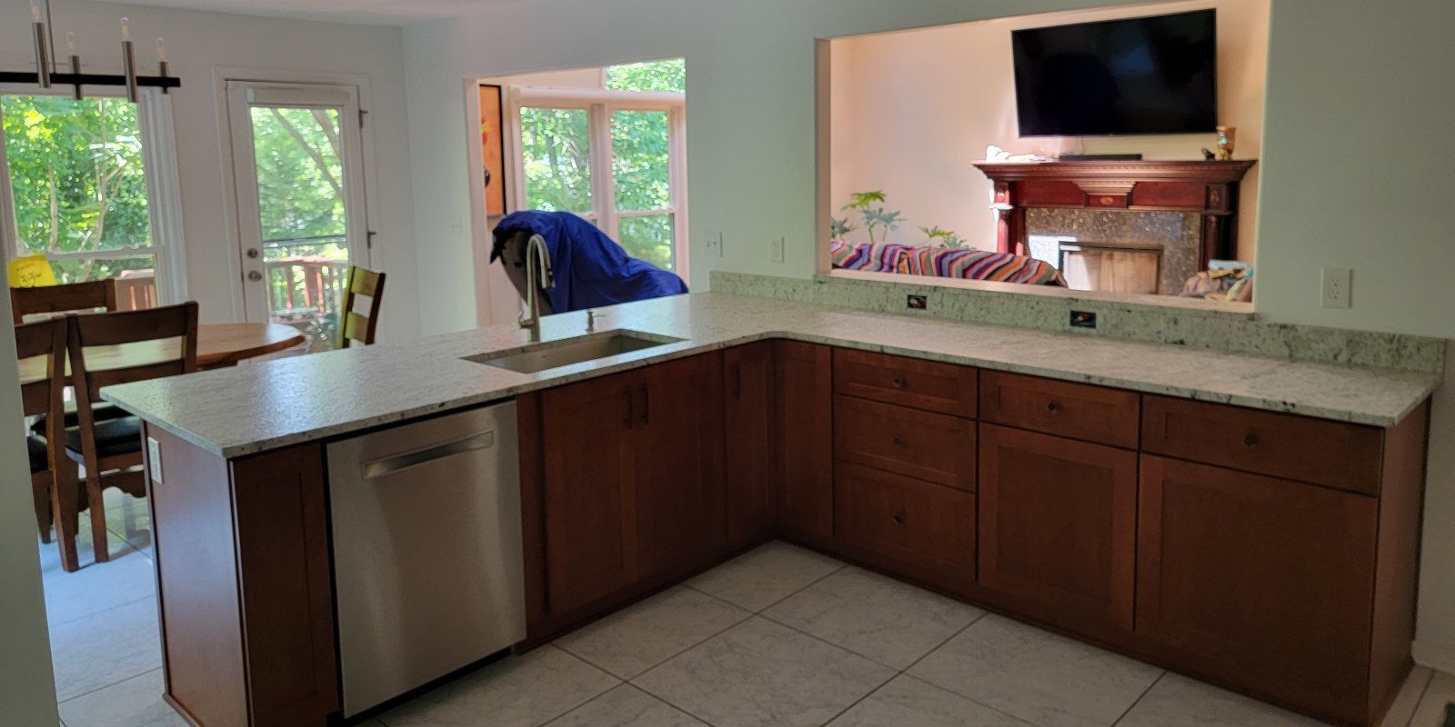 Modern kitchen with dark wood cabinets, granite island, and a person cleaning near the bright window.