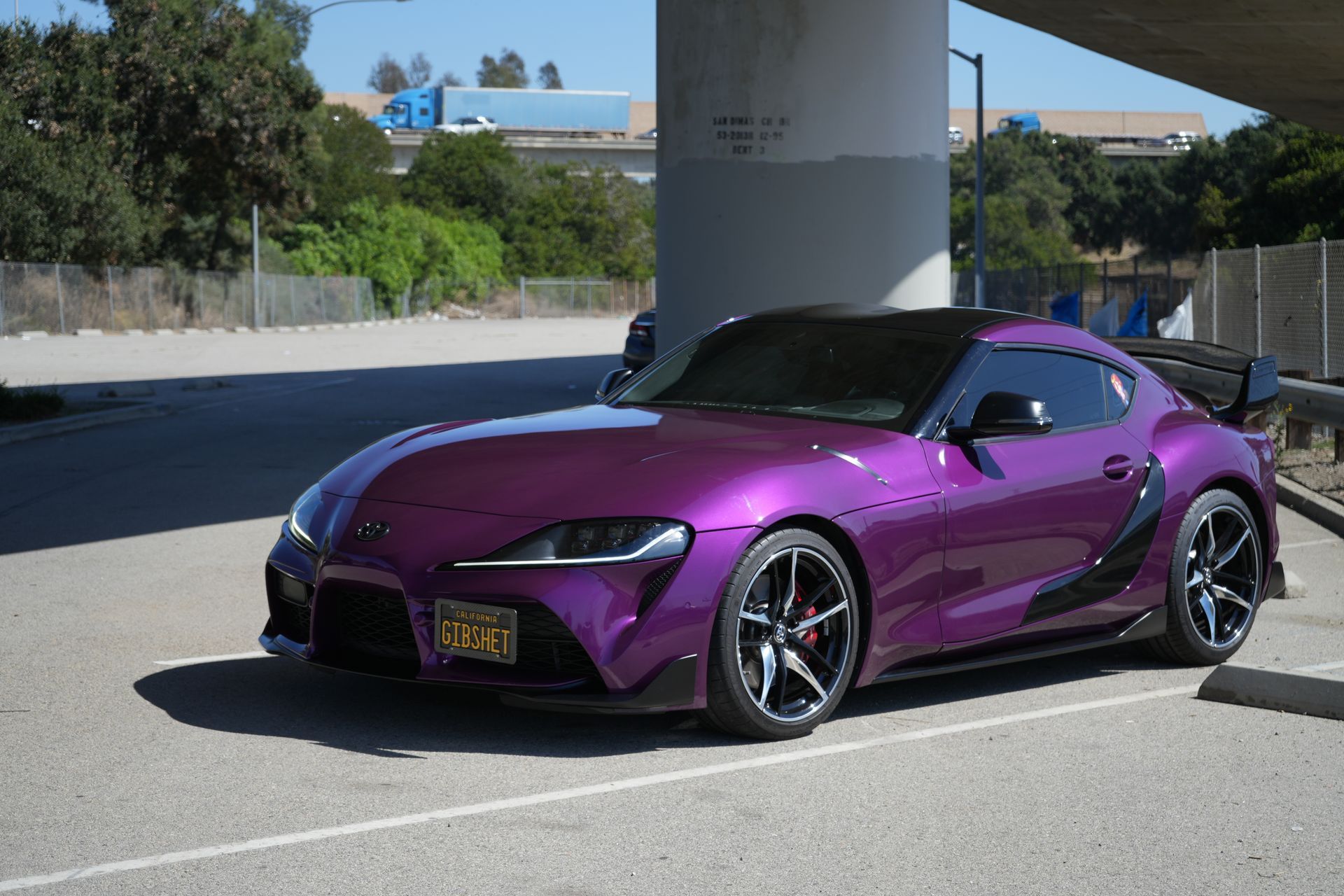A purple sports car is parked under a bridge in a parking lot.