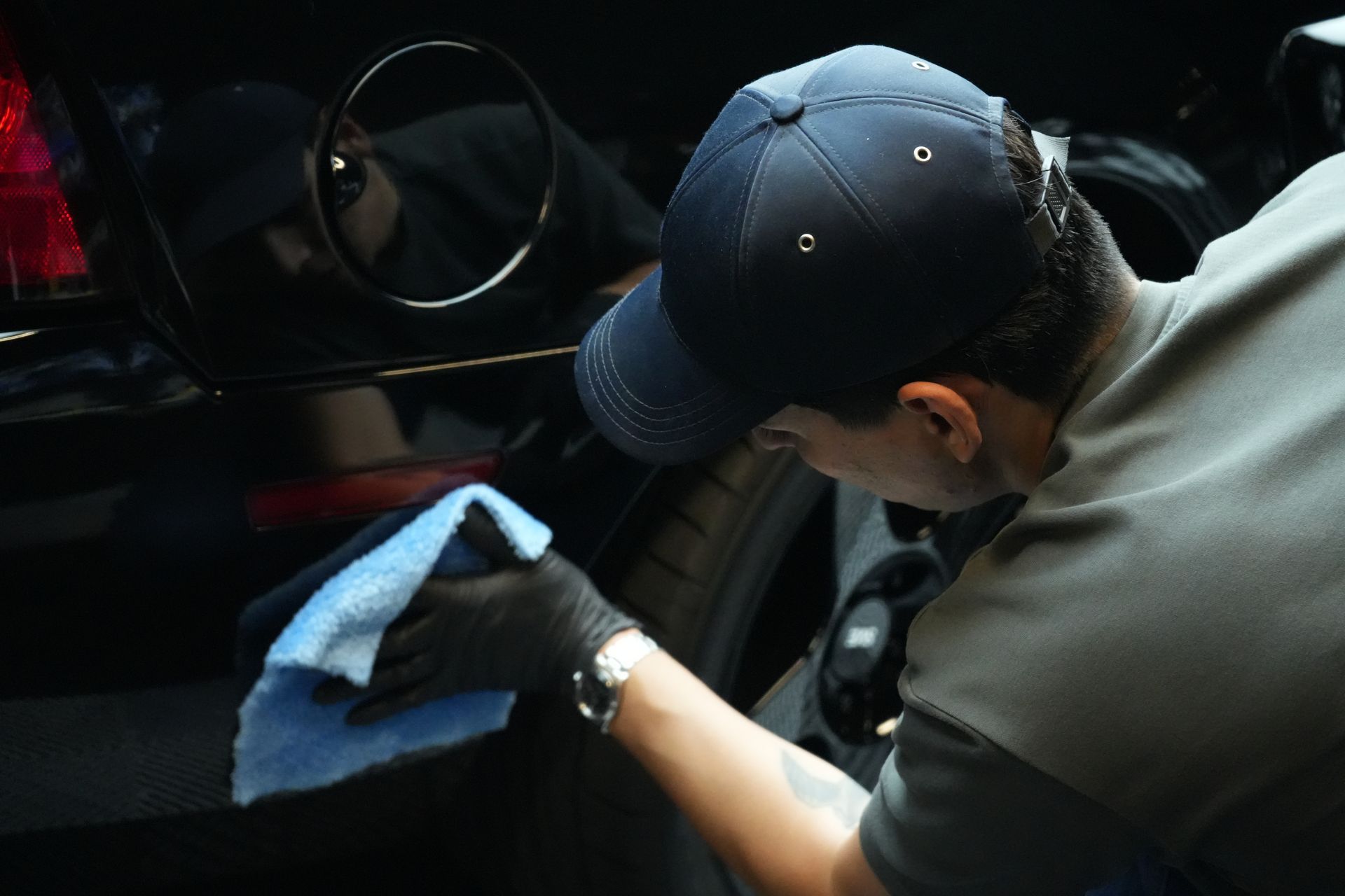 A man in a baseball cap is cleaning a car with a cloth