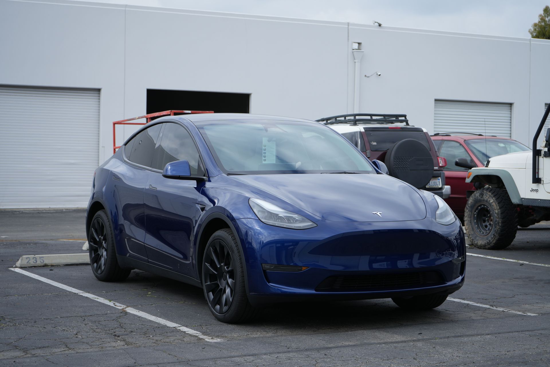 A blue tesla model y is parked in a parking lot in front of a building.