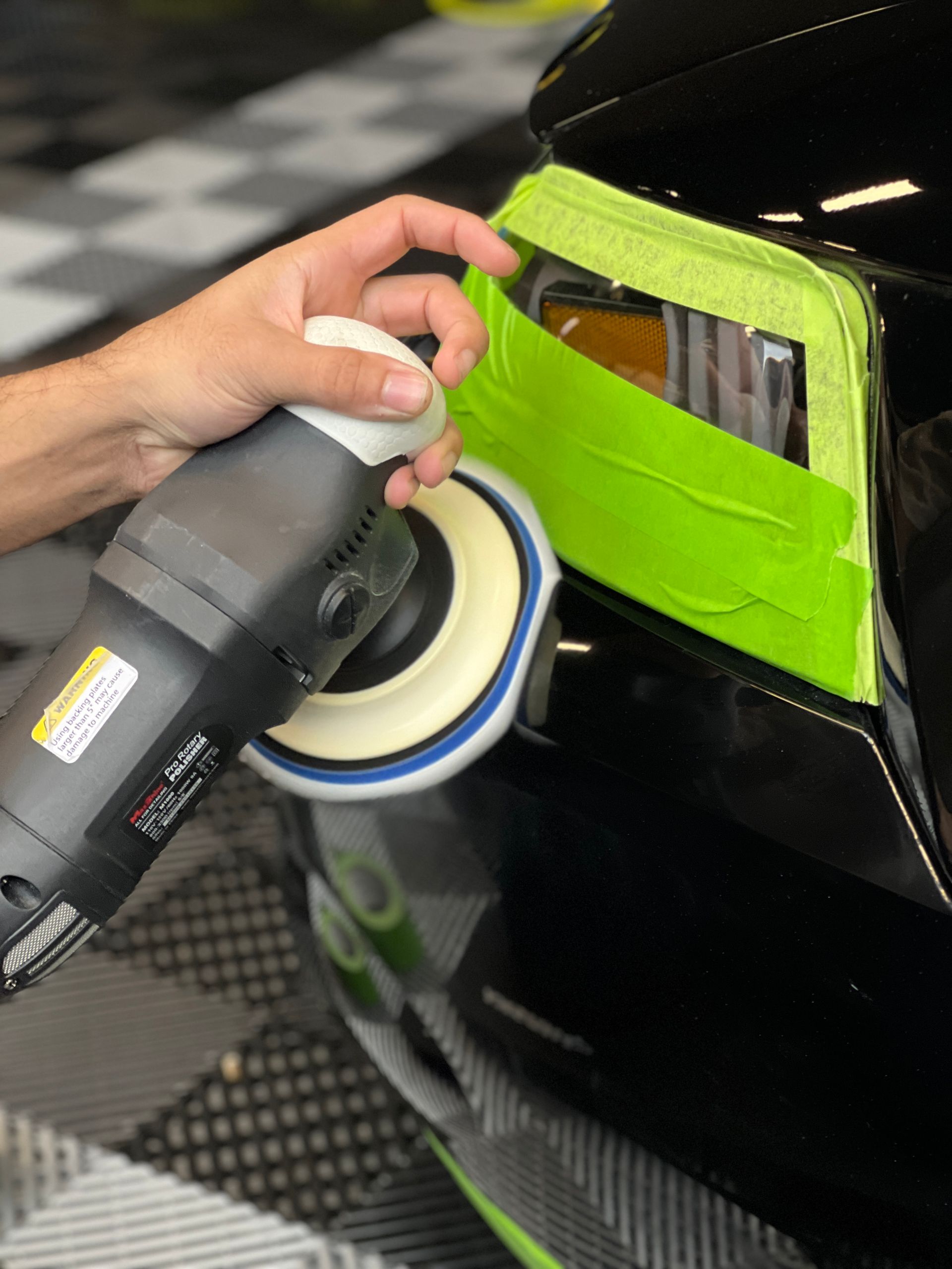 A person is polishing a black car with a machine.