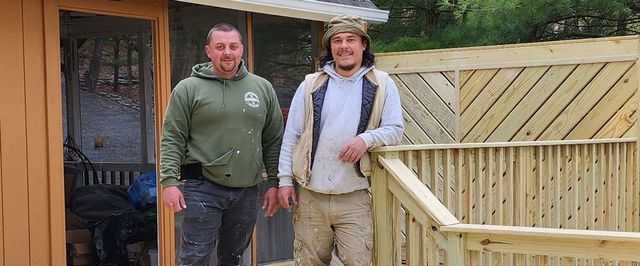 Two men are standing next to each other on a wooden deck.