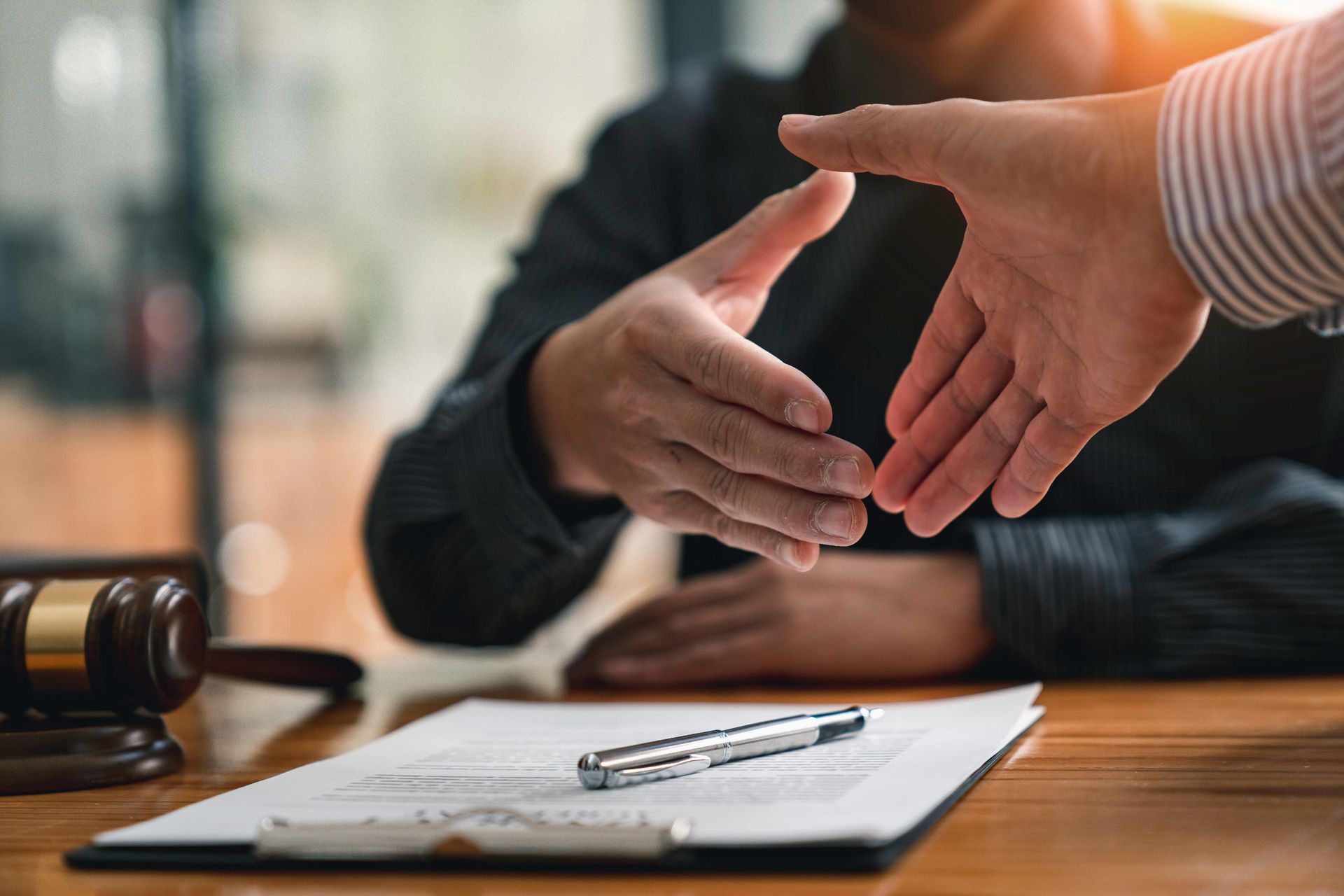 Handshake over signed documents with pen and judge’s gavel on a desk.