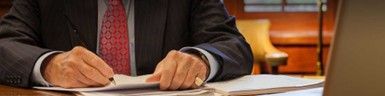 A person in a suit writing on paper with a pen at a desk. A person in a suit writing on paper with a pen at a desk.