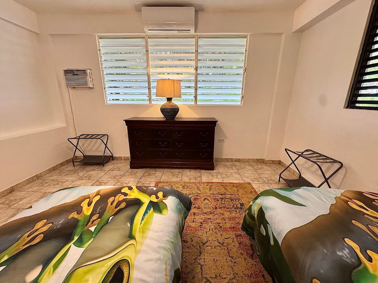 Bedroom with two twin beds, a wooden chest, and a window with blinds.