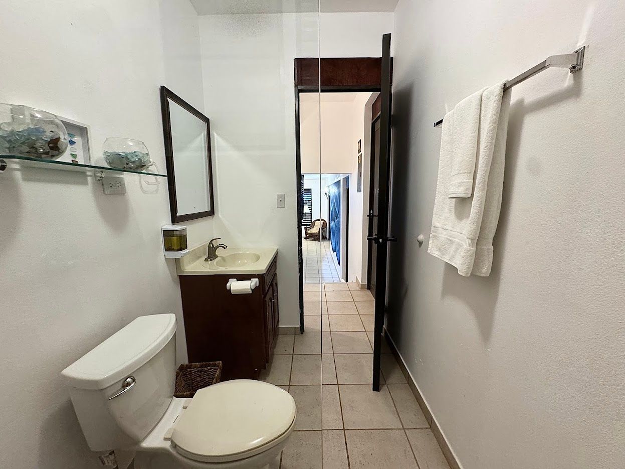 A small bathroom with a toilet, sink, mirror, and towel rack; an open door leads to a hallway.