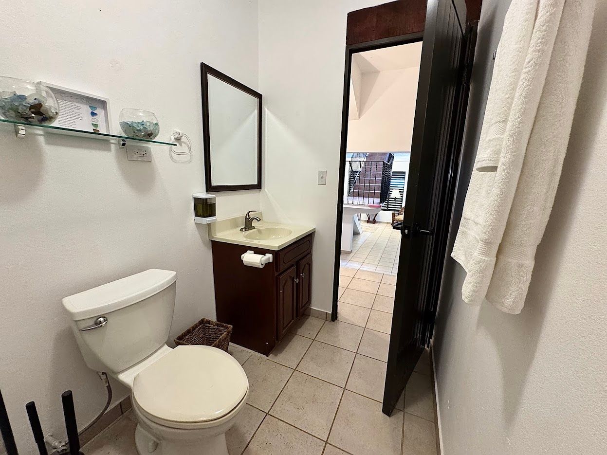 Small bathroom with toilet, vanity, and open doorway to another room. A towel hangs on the door.