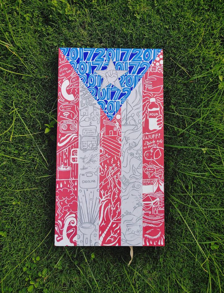A handmade Puerto Rican flag on grass, featuring intricate hand-drawn patterns and text over the red, white, and blue.