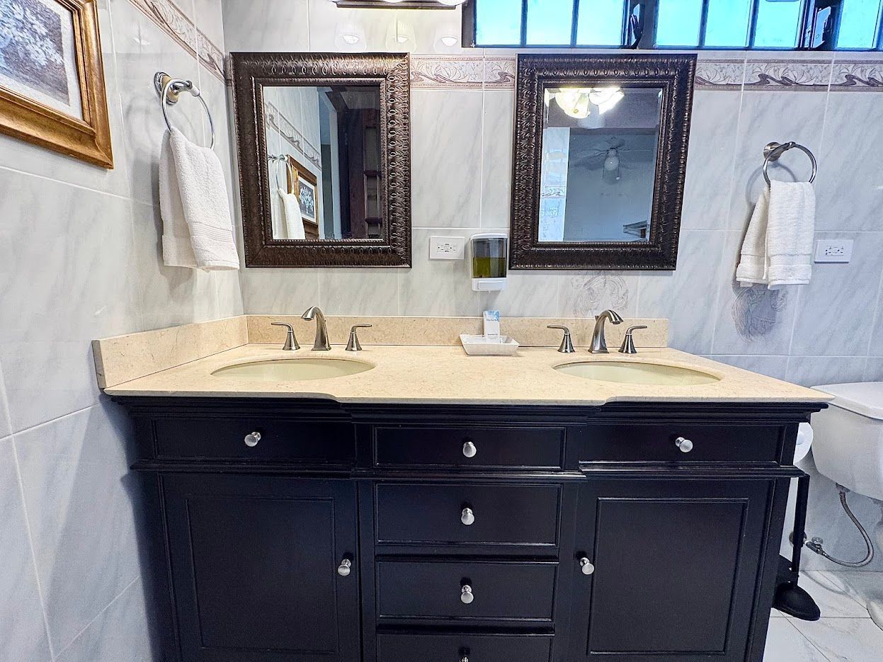Bathroom vanity with dual sinks, mirrors, and towels; black cabinet with light countertop.