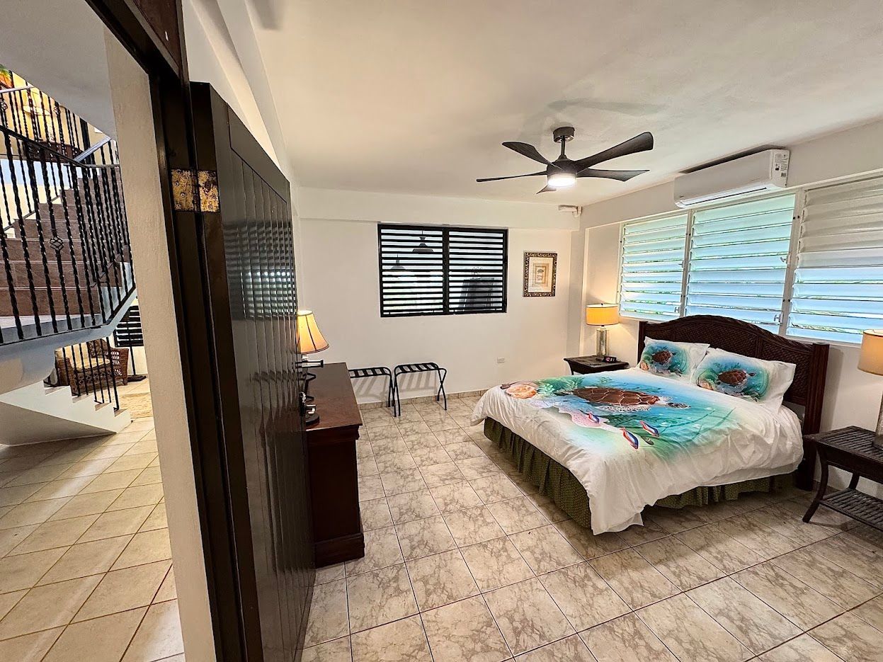 Bedroom with brown furniture, a bed with blue accents, and tiled floors. A window is on the right side.