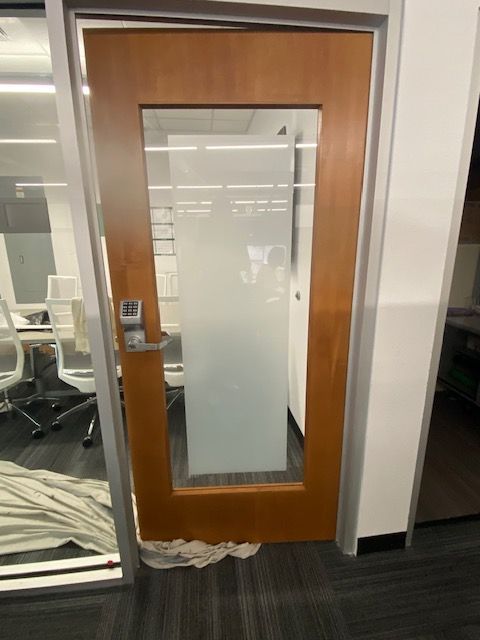Wooden office door with frosted glass panel beside a conference room with glass walls