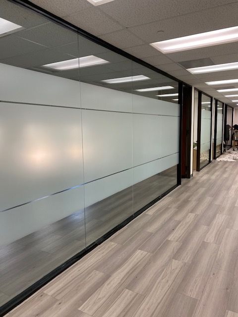 Modern office hallway with frosted glass walls, wood flooring, and ceiling lights