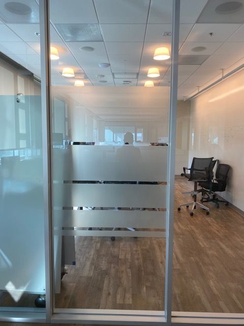 Modern office conference room with glass walls, wood floor, and black chairs.