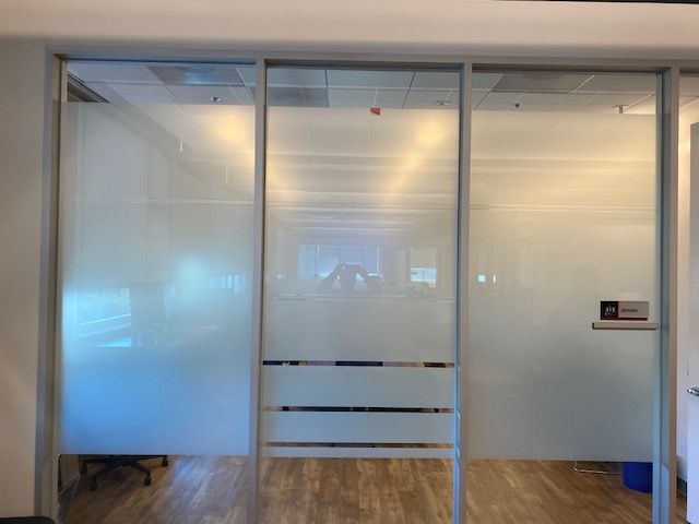 Office hallway with frosted glass doors and a wood floor, seen from outside a conference room.