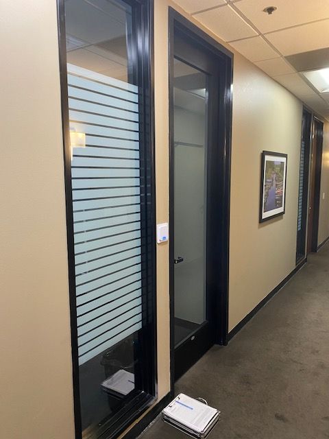Office hallway with a glass-paneled door, framed wall art, and a clipboard on the floor.