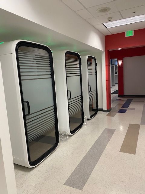 Modern office hallway with frosted glass pods, white walls, red accent wall, and gray floor stripes