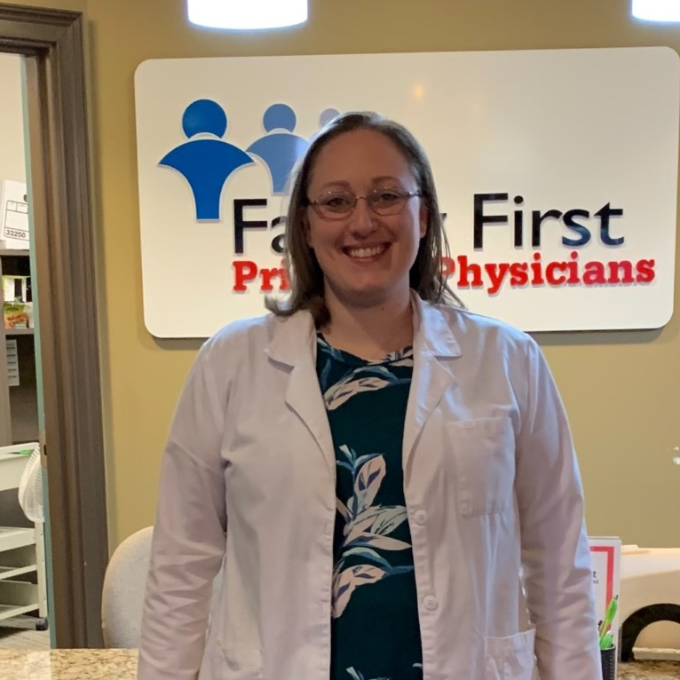 Woman in lab coat smiles in front of 