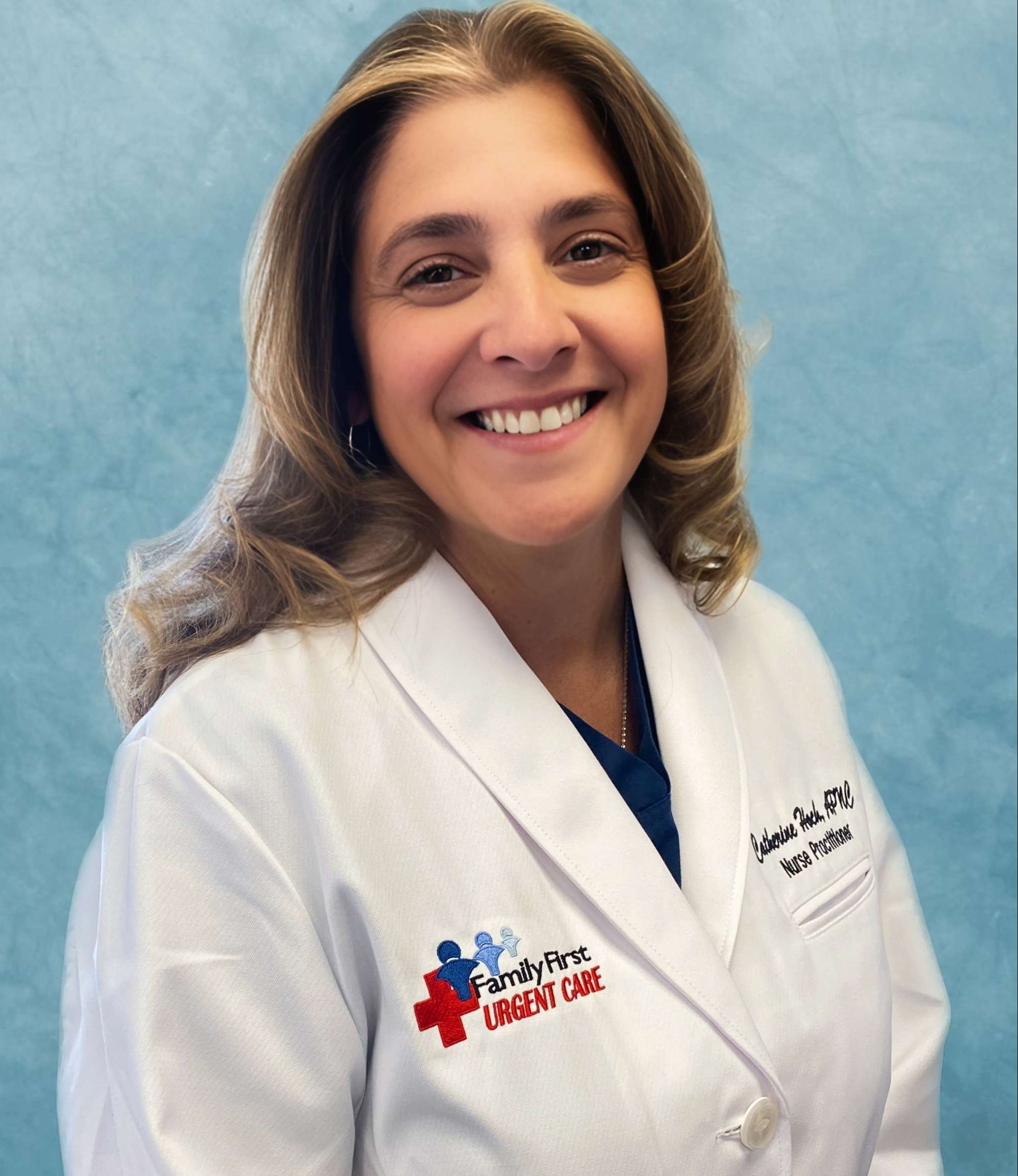 Woman with blonde hair in white coat smiles, “Family First Urgent Care” logo on chest.