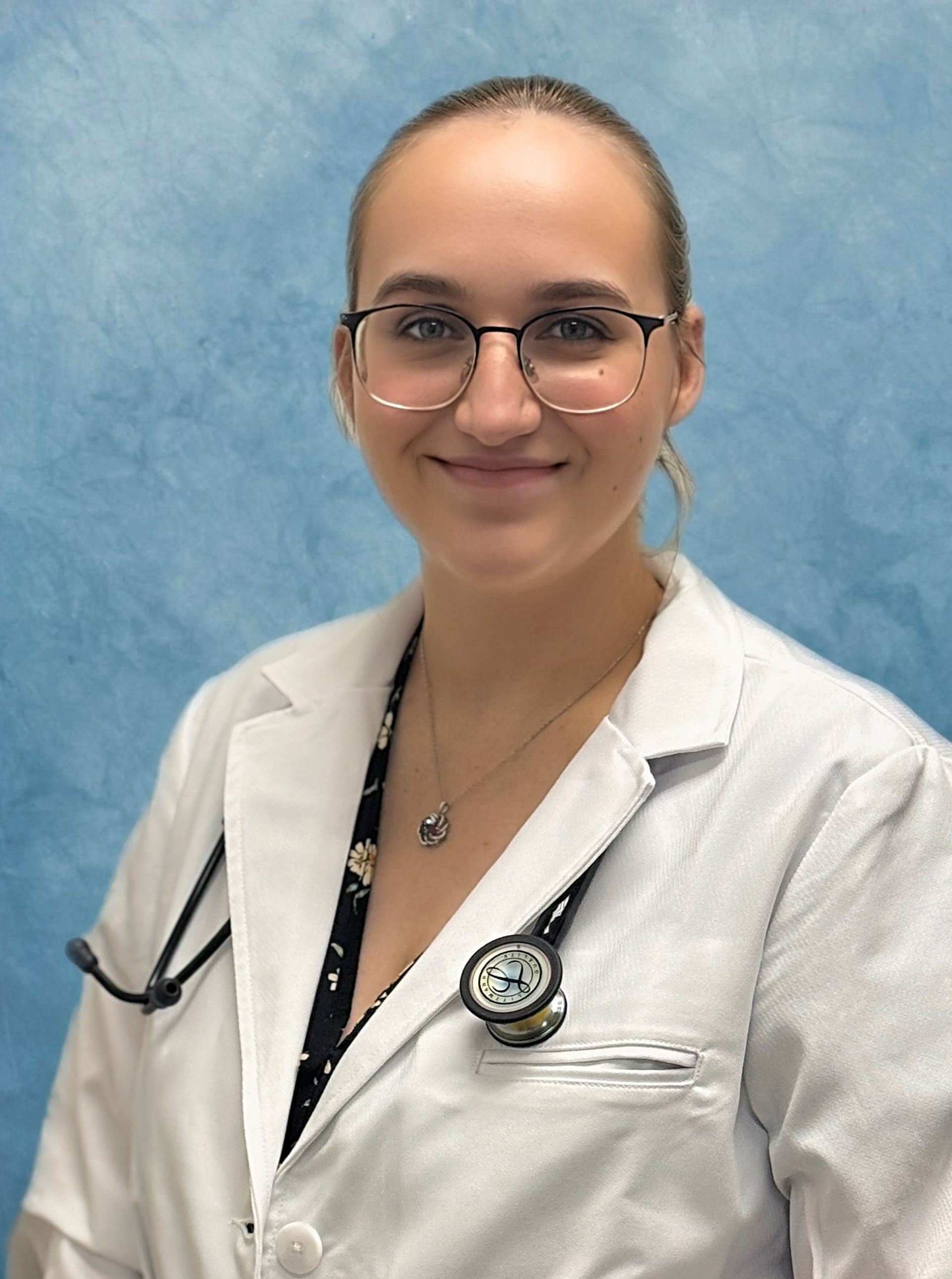 Woman in white coat with stethoscope, smiling, wearing glasses. Blue background.