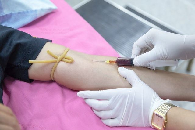 Person getting blood drawn at medical facility. Arm with tourniquet, needle, medical professional in gloves.