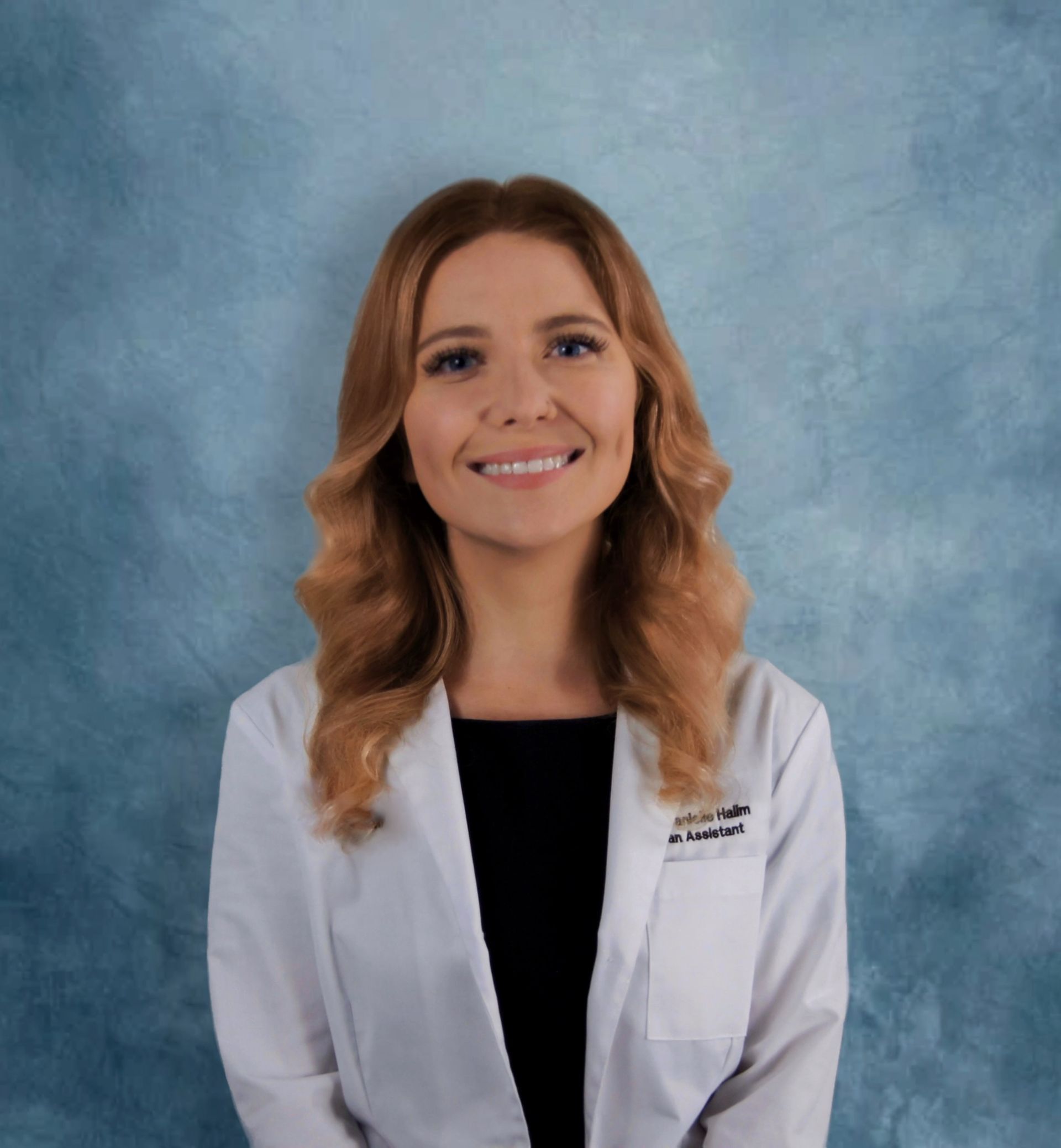 Woman in a white coat smiling, standing in front of a blue backdrop.