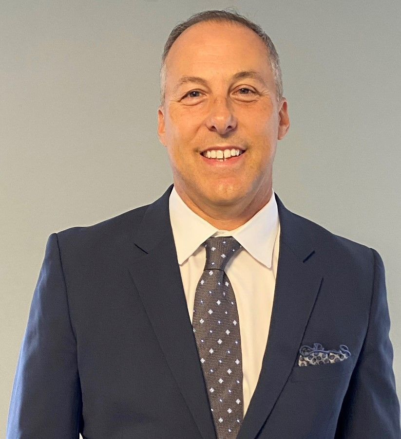 Man in dark suit, smiling, wearing a tie and white collared shirt.