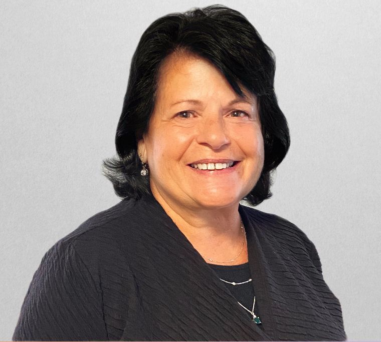 Woman with dark hair smiles, wearing a black shirt and necklace against a light grey background.