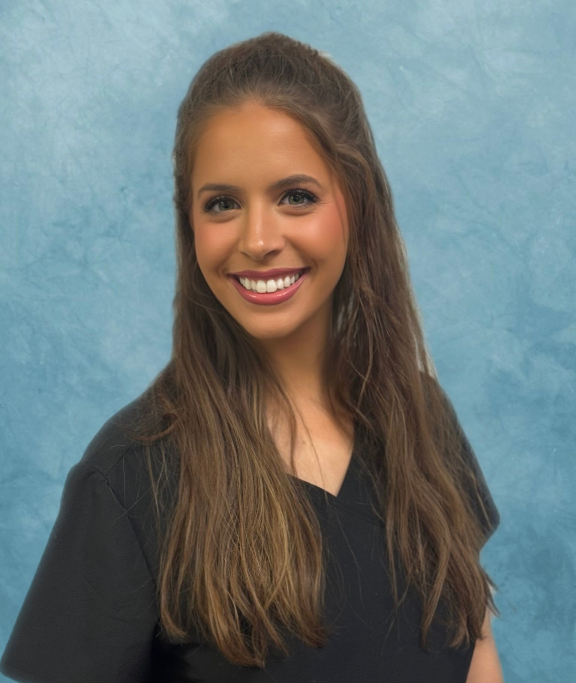 Woman smiling, long brown hair, wearing a black shirt, blue background.
