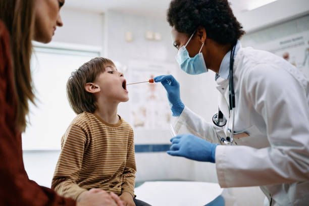 Doctor examining a child’s throat with a swab in a clinic, while a parent watches nearby.