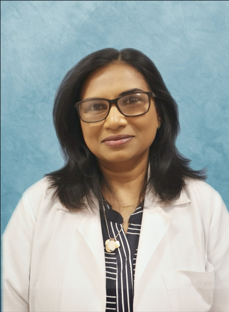 Woman in a white coat smiling, standing in front of a blue backdrop.