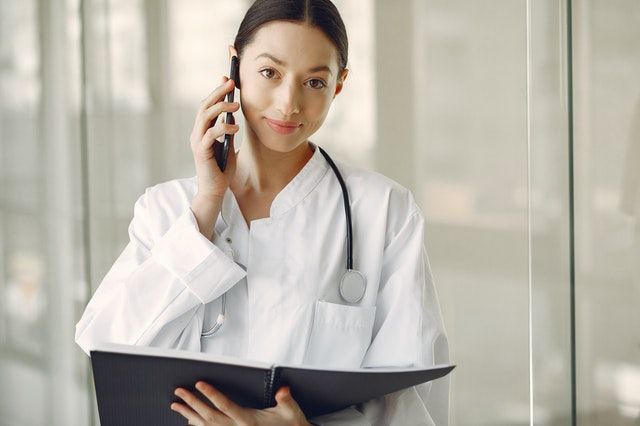 Doctor in white coat holds phone and folder, looks at the camera.